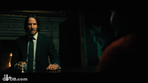 A Man In A Suit And Tie Is Sitting At A Table With The Number 18 On The Bottom Right GIF