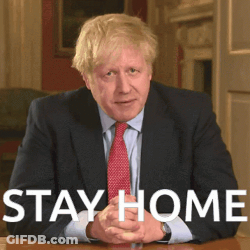 A Man In A Suit And Tie Is Sitting At A Table With The Words " Stay Home " Written Above Him GIF