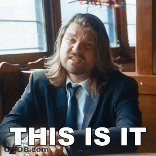 A Man In A Suit And Tie Is Sitting At A Table With The Words " This Is It " Written Below Him GIF