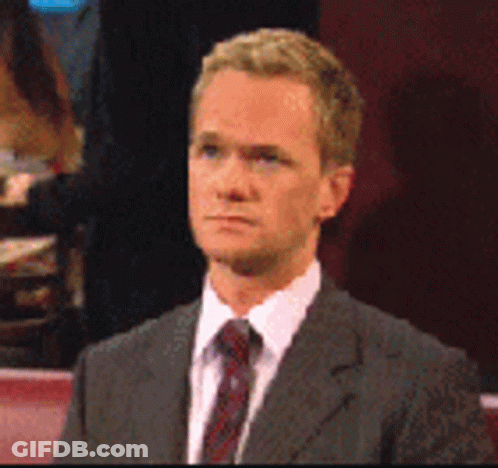 A Man In A Suit And Tie Is Sitting Down GIF