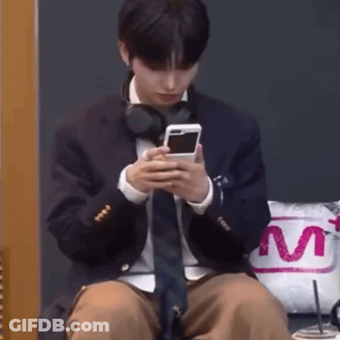 A Man In A Suit And Tie Is Sitting Down Looking At His Phone . GIF