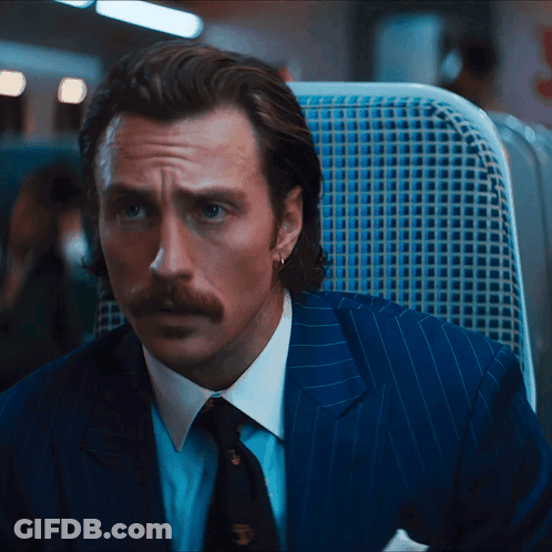 A Man In A Suit And Tie Is Sitting In A Blue Chair GIF