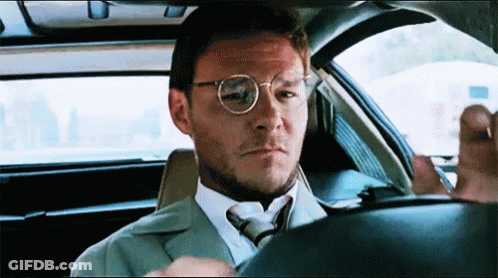 A Man In A Suit And Tie Is Sitting In A Car Looking Out The Window . GIF