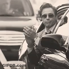 A Man In A Suit And Tie Is Sitting In A Car Waving His Hand . GIF