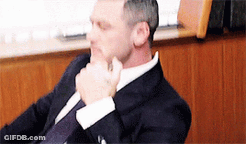 A Man In A Suit And Tie Is Sitting In A Chair . GIF