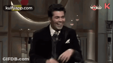 A Man In A Suit And Tie Is Sitting In A Chair And Laughing . GIF