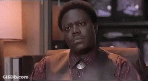 A Man In A Suit And Tie Is Sitting In A Chair And Looking At The Camera . GIF