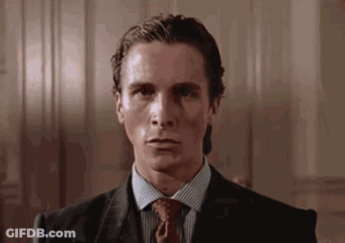 A Man In A Suit And Tie Is Sitting In A Chair And Looking At The Camera . GIF