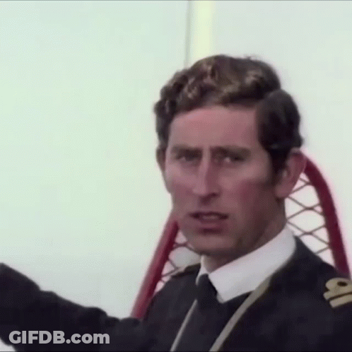 A Man In A Suit And Tie Is Sitting In A Chair And Looking At The Camera . GIF