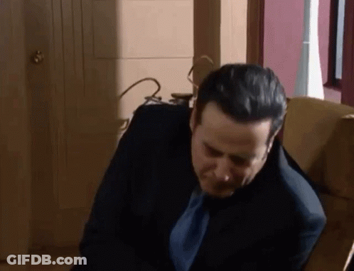 A Man In A Suit And Tie Is Sitting In A Chair And Looking Down . GIF