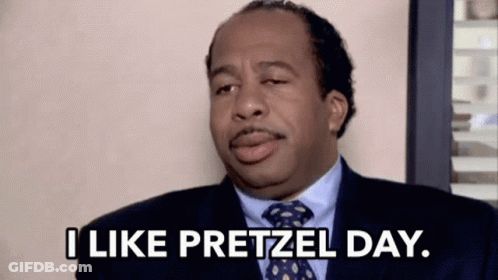 A Man In A Suit And Tie Is Sitting In A Chair And Saying `` I Like Pretzel Day . '' GIF