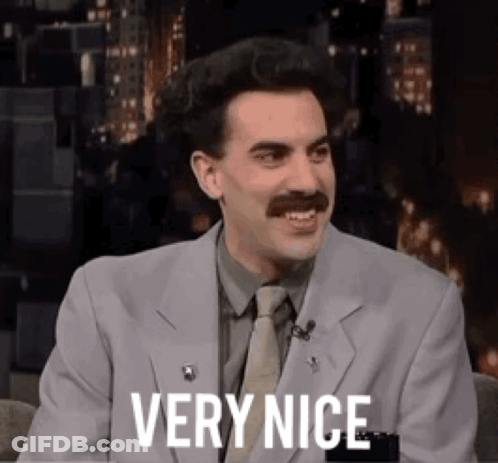 A Man In A Suit And Tie Is Sitting In A Chair And Smiling . GIF