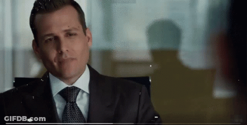 A Man In A Suit And Tie Is Sitting In A Chair And Smiling . GIF