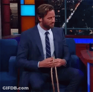 A Man In A Suit And Tie Is Sitting In A Chair And Tying A Rope . GIF