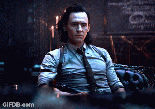 A Man In A Suit And Tie Is Sitting In A Chair In A Dark Room GIF
