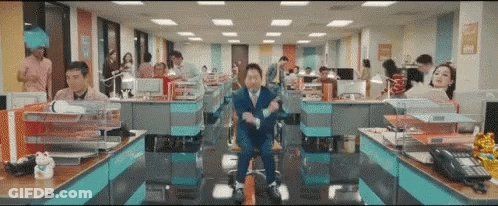 A Man In A Suit And Tie Is Sitting In A Chair In An Office Surrounded By People . GIF