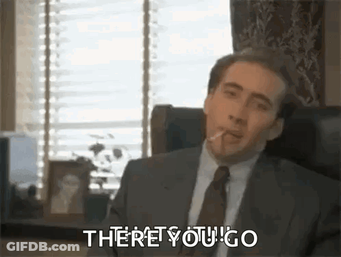 A Man In A Suit And Tie Is Sitting In A Chair Smoking A Cigarette And Saying `` There You Go '' . GIF