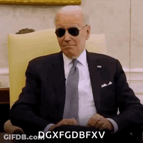 A Man In A Suit And Tie Is Sitting In A Chair Wearing Sunglasses And Making A Funny Face . GIF