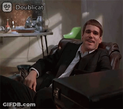 A Man In A Suit And Tie Is Sitting In A Chair With A Briefcase Next To Him .. GIF