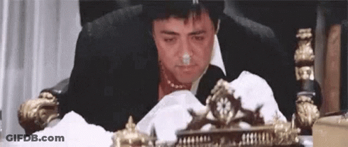 A Man In A Suit And Tie Is Sitting In A Chair With A Napkin In His Nose . GIF