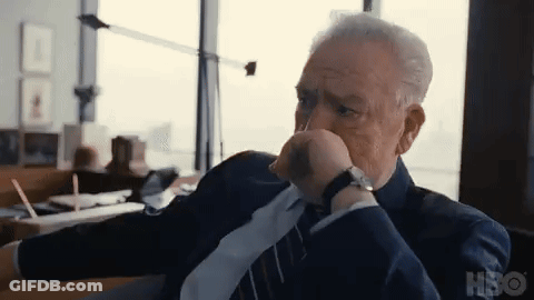 A Man In A Suit And Tie Is Sitting In A Chair With His Hand On His Chin . GIF