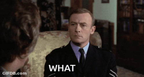 A Man In A Suit And Tie Is Sitting In A Chair With The Word What Written Below Him GIF
