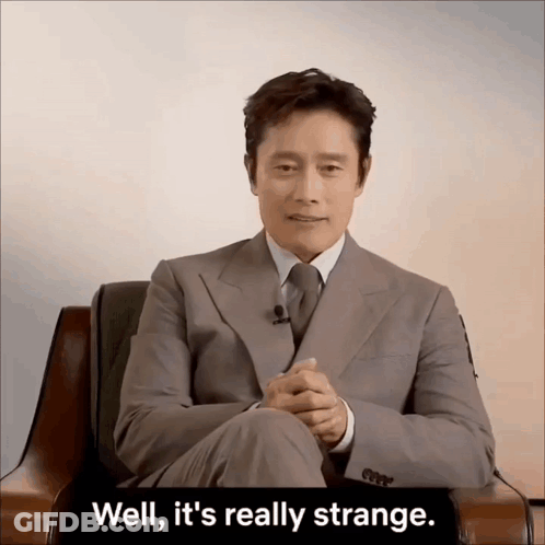 A Man In A Suit And Tie Is Sitting In A Chair With The Words Well It 'S Really Strange Behind Him GIF