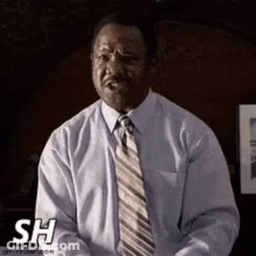 A Man In A Suit And Tie Is Sitting In A Chair . GIF
