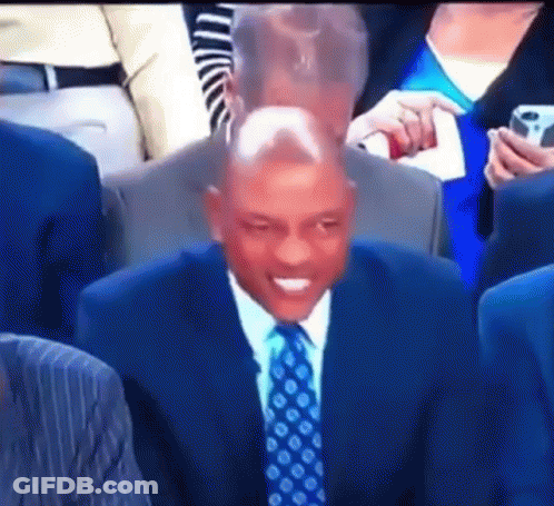 A Man In A Suit And Tie Is Sitting In A Crowd GIF