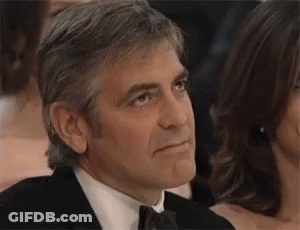 A Man In A Suit And Tie Is Sitting In A Crowd Of People And Looking To The Side . GIF
