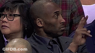 A Man In A Suit And Tie Is Sitting In A Crowd Of People And Pointing . GIF