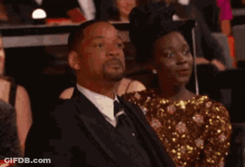 A Man In A Suit And Tie Is Sitting In A Crowd Of People . GIF
