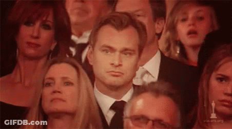 A Man In A Suit And Tie Is Sitting In A Crowd Of People Watching A Movie . GIF