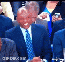 A Man In A Suit And Tie Is Sitting In A Crowd With His Tongue Out GIF