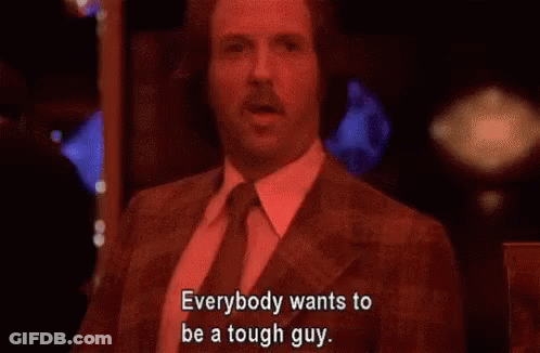 A Man In A Suit And Tie Is Sitting In A Dark Room And Says Everybody Wants To Be A Tough Guy . GIF