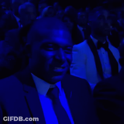 A Man In A Suit And Tie Is Sitting In A Dark Room Under Blue Lights GIF