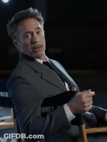 A Man In A Suit And Tie Is Sitting In A Director 'S Chair That Says Pascal On It GIF