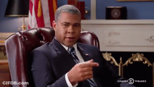 A Man In A Suit And Tie Is Sitting In A Leather Chair And Pointing GIF