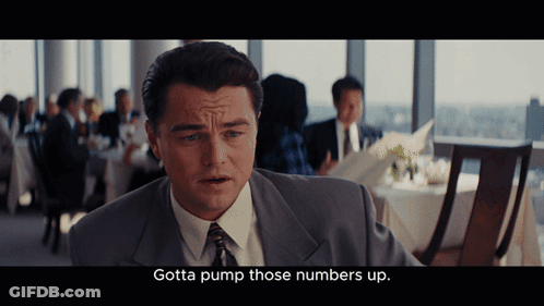 A Man In A Suit And Tie Is Sitting In A Restaurant And Says Gotta Pump Those Numbers Up GIF