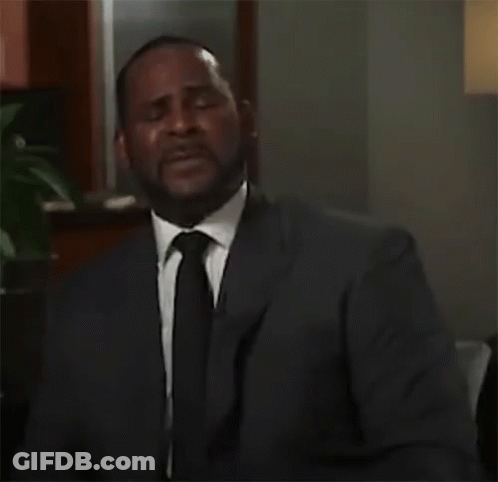 A Man In A Suit And Tie Is Sitting In A Room . GIF