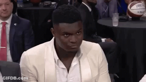 A Man In A Suit And Tie Is Sitting In A Room With Other People . GIF