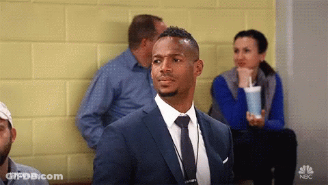 A Man In A Suit And Tie Is Sitting In A Waiting Room With Other People . GIF