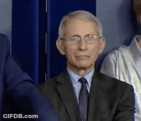 A Man In A Suit And Tie Is Sitting In Front Of A Blue Wall . GIF