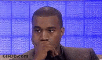 A Man In A Suit And Tie Is Sitting In Front Of A Blue Wall . GIF