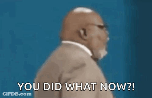 A Man In A Suit And Tie Is Sitting In Front Of A Blue Wall . GIF