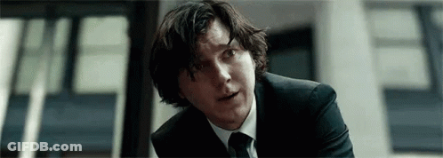 A Man In A Suit And Tie Is Sitting In Front Of A Building . GIF