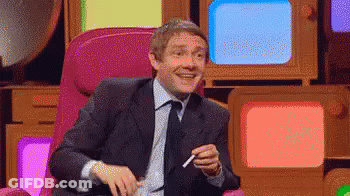 A Man In A Suit And Tie Is Sitting In Front Of A Bunch Of Televisions And Smoking A Cigarette . GIF