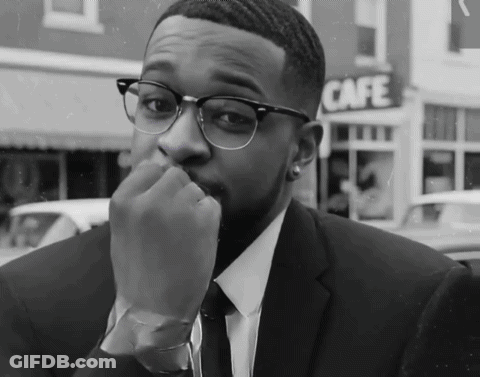 A Man In A Suit And Tie Is Sitting In Front Of A Cafe Sign GIF