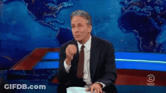A Man In A Suit And Tie Is Sitting In Front Of A Comedy Central Sign GIF