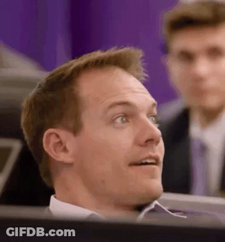 A Man In A Suit And Tie Is Sitting In Front Of A Computer Screen Looking Up . GIF
